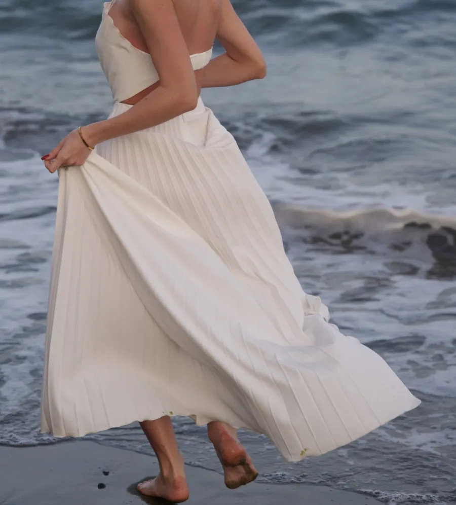 Le plissé de la robe longue blanche Shell de REPULO'S s'ouvre en mouvement au bord de la mer